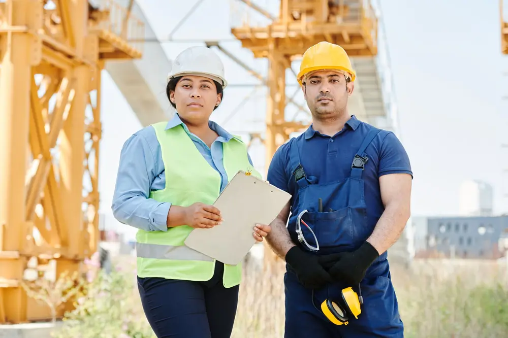 Two engineers in hard hats reviewing plans on a construction site